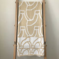 Eclectic sand and white cotton tablecloth featuring a bold abstract pattern draped over a wooden ladder