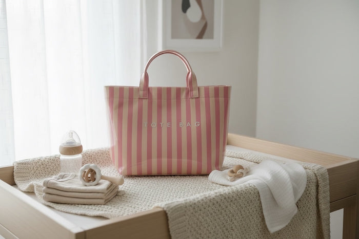 Eclectic blush and neutral stripe PVC carry tote bag on a nursery changing table with baby essentials.
