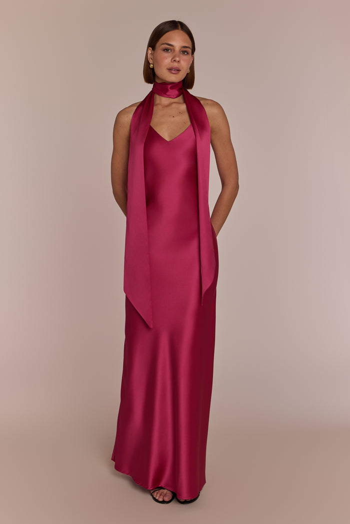 Woman wearing a long pink dress with a matching scarf on a beige background