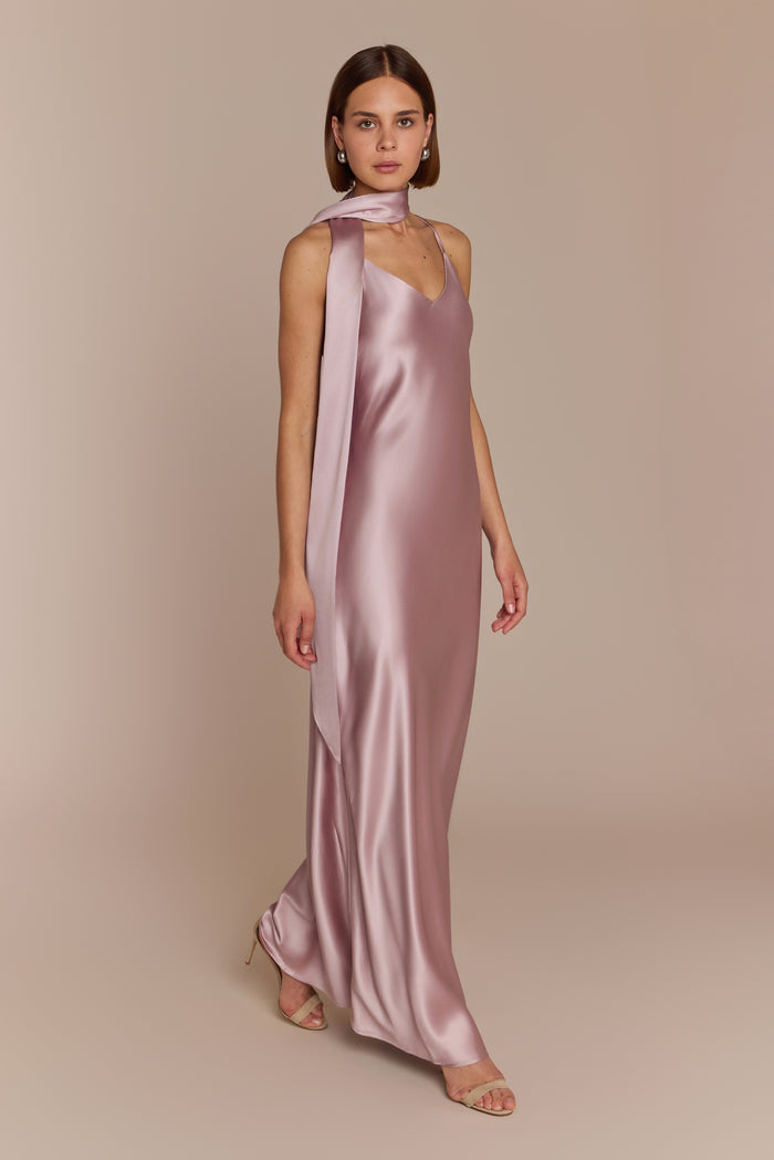 Woman wearing a pink satin bridesmaid gown with a long train on a beige background