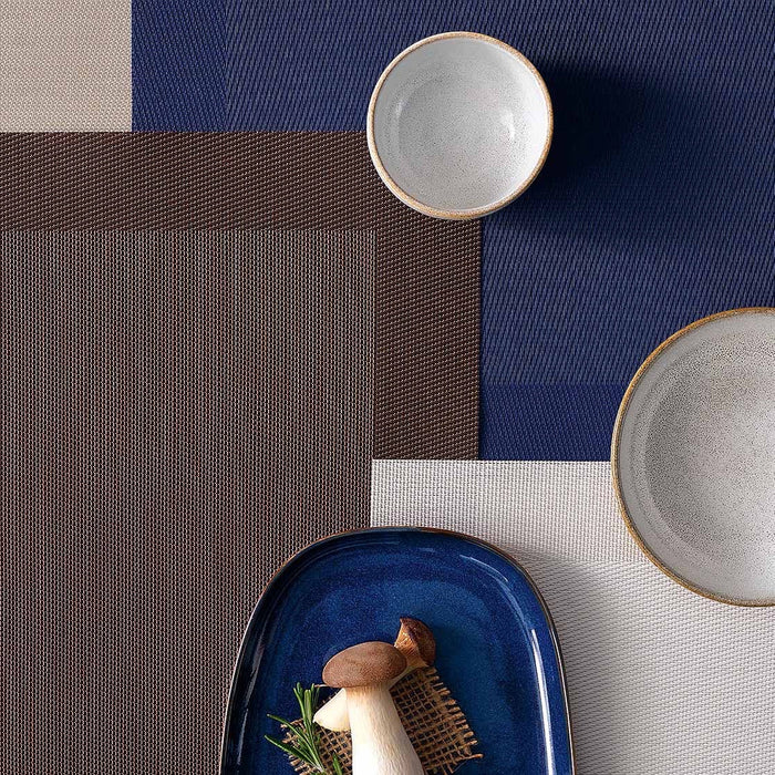 Eclectic ASA Selection brown PVC placemat with woven texture layered with blue and beige mats and ceramic bowls
