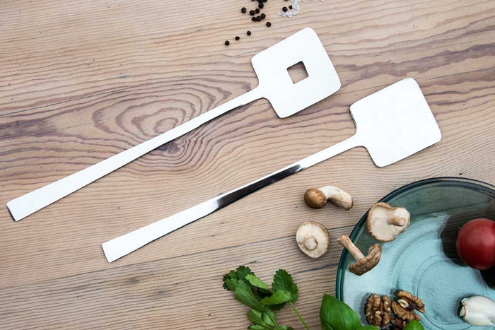 Eclectic Deco geometric stainless steel salad servers with a polished mirror finish on a wooden table