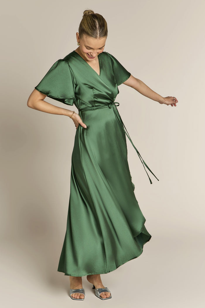 Woman wearing a green satin bridesmaid dress against a beige background