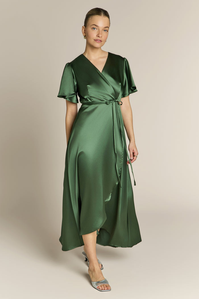 Woman wearing a green satin wrap bridesmaid dress against a beige background