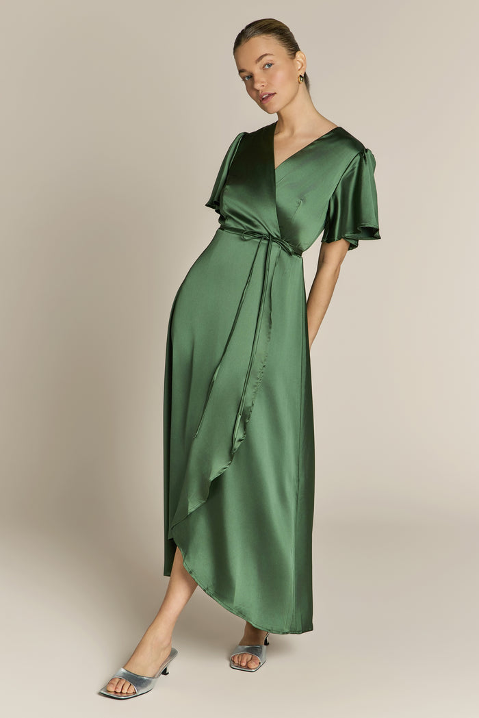 Woman wearing a green satin bridesmaid dress against a plain background