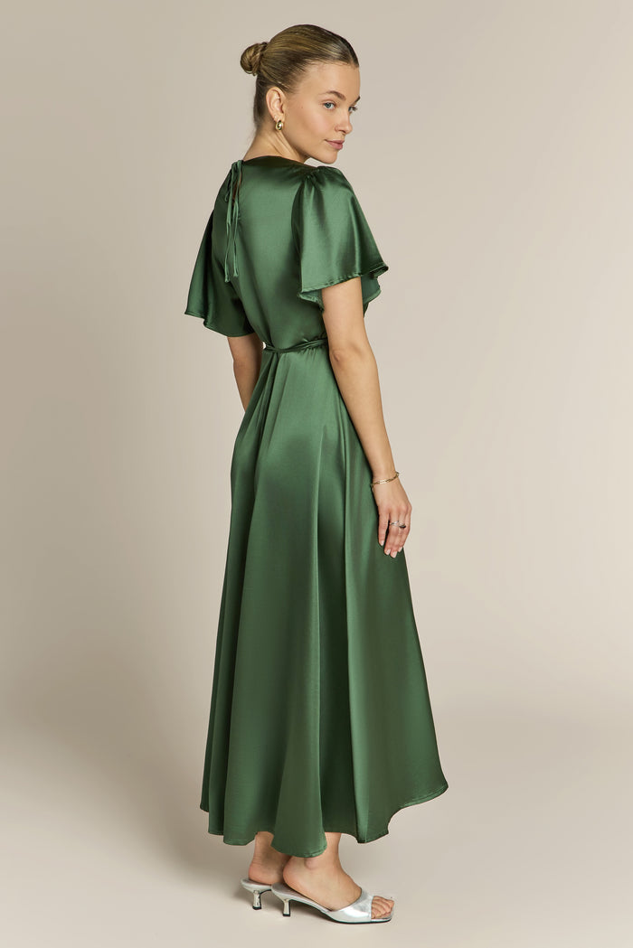 Woman wearing a green dress with ruffled sleeves on a beige background