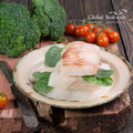 Pacific cod fillet portions on a plate with green leaves, with broccoli and tomatoes behind.