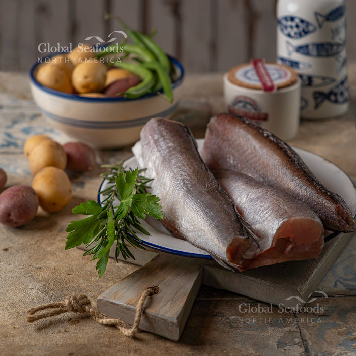 Headed and tailed Pacific whiting on a board with potatoes and parsley nearby.