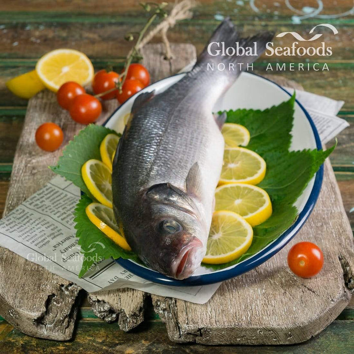 Whole branzino on a blue plate with lemon slices and green leaves.