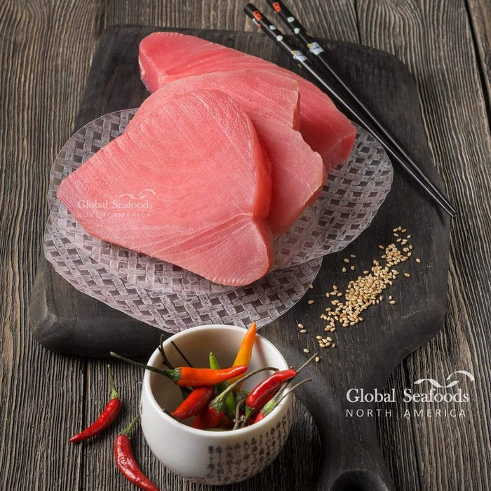 Three raw yellowfin tuna steaks on a patterned plate with chopsticks and chili peppers