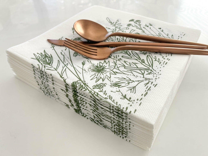 Eclectic Fynbos sage green disposable airlaid napkins with botanical print, topped with copper cutlery on white table.