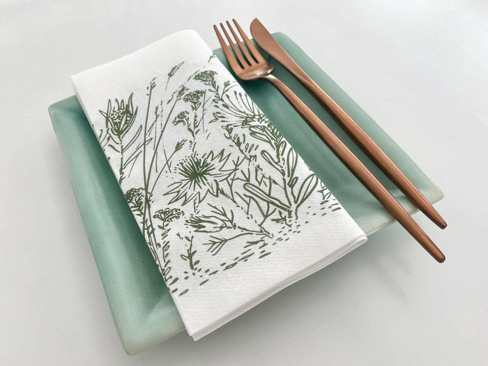 Eclectic Fynbos sage green airlaid napkin with botanical print on a ceramic plate with copper cutlery