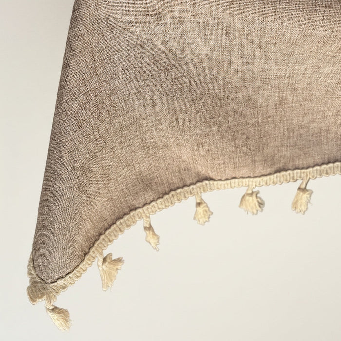 Eclectic light coffee linen blend tablecloth featuring a textured fabric finish and decorative cream tassel trim.