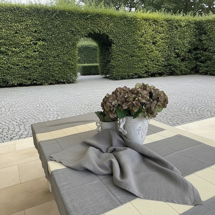 Eclectic ash grey linen-look polyester table runner draped on an outdoor table with a flower pot in a garden setting.