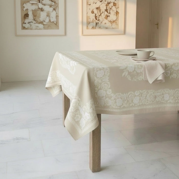 Eclectic beige linen-look tablecloth with an intricate white floral border draped over a dining table.