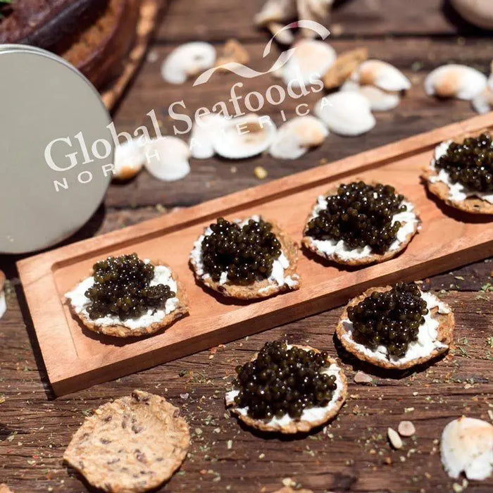Side view of a cracker topped with cream and Paddlefish caviar, placed on a wooden board, showcasing the texture and gourmet appeal of this refined seafood appetizer
