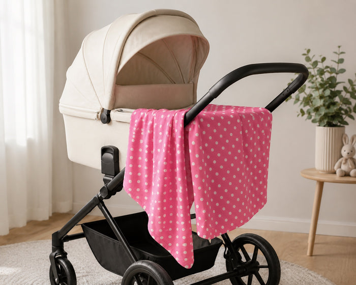 Eclectic pink cotton flannel baby blanket with white polka dots draped over a cream-colored pram in a nursery.