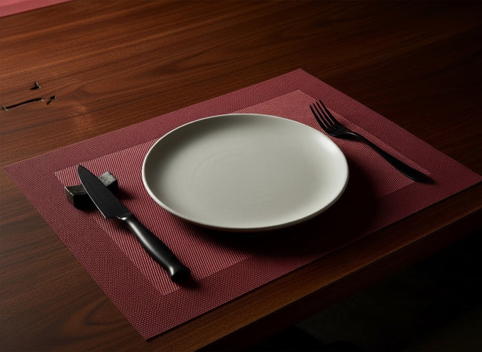 Eclectic ASA Selection pomegranate red PVC placemat with woven texture on a dark wooden table with a white plate.