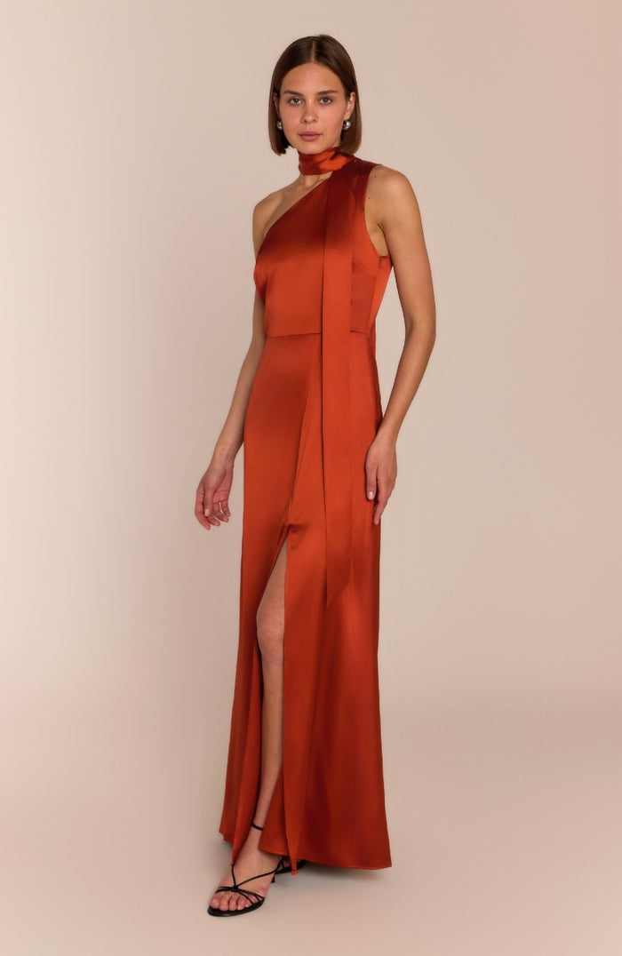 Woman wearing a rust-colored halter neck gown with a high slit on a beige background