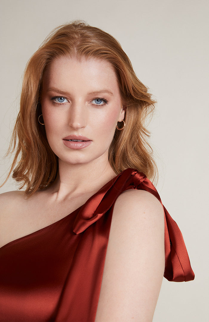 Woman wearing a burnt orange satin dress against a neutral background