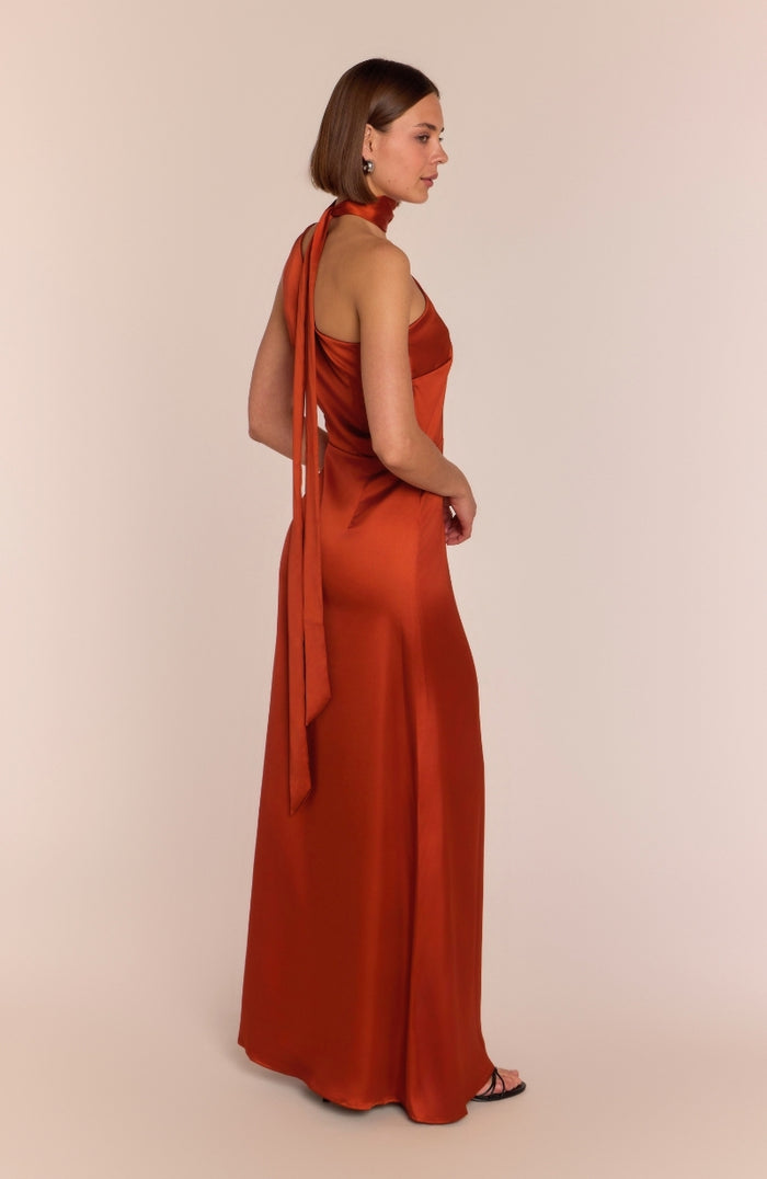 Woman wearing a rust-colored halter neck dress with a long train on a beige background