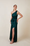 Woman wearing a dark green one-shoulder dress with a slit on a beige background
