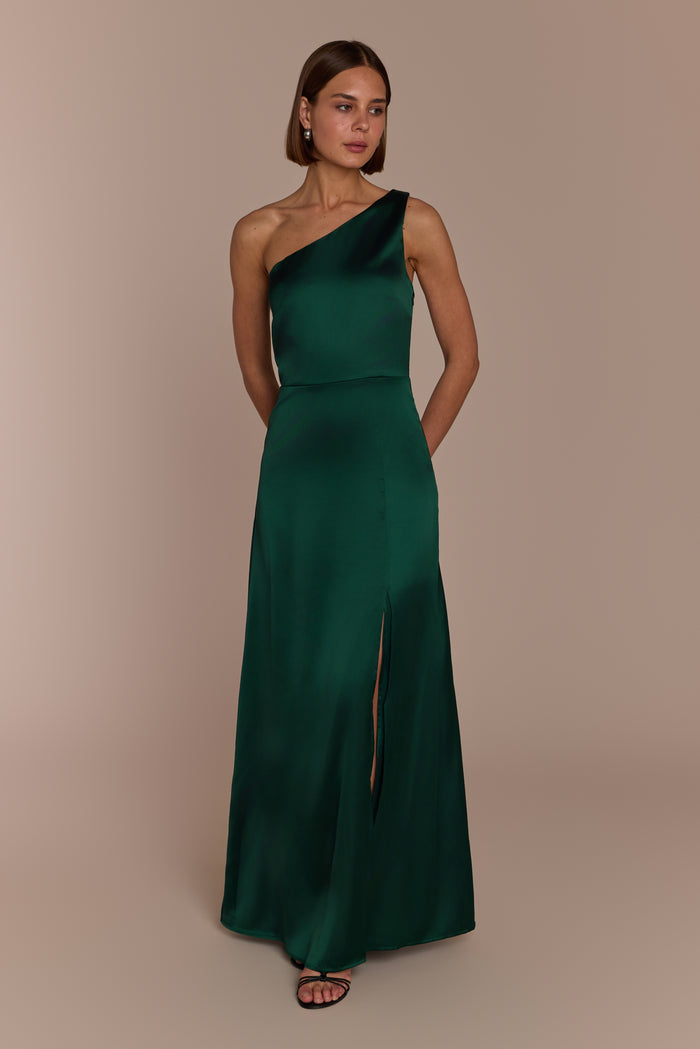 Woman wearing a forest green one-shoulder bridesmaid dress against a beige background