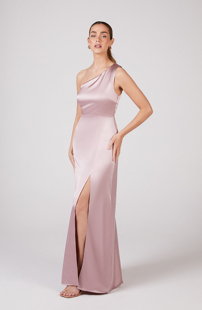 Woman wearing a pink one-shoulder evening gown with a slit on a white background