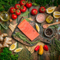 Overhead view of coho salmon portions on a wooden board with tomatoes, herbs and lemon