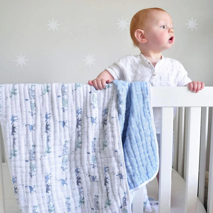 Eclectic Aden + Anais Rising Star muslin dream blanket draped over a white cot with a toddler standing inside