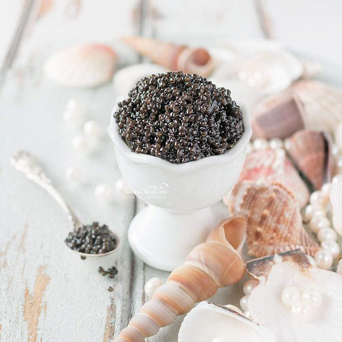 Siberian Sturgeon caviar served in a white cup with a silver spoon holding caviar beside it, surrounded by sea shells for a refined and coastal-inspired presentation
