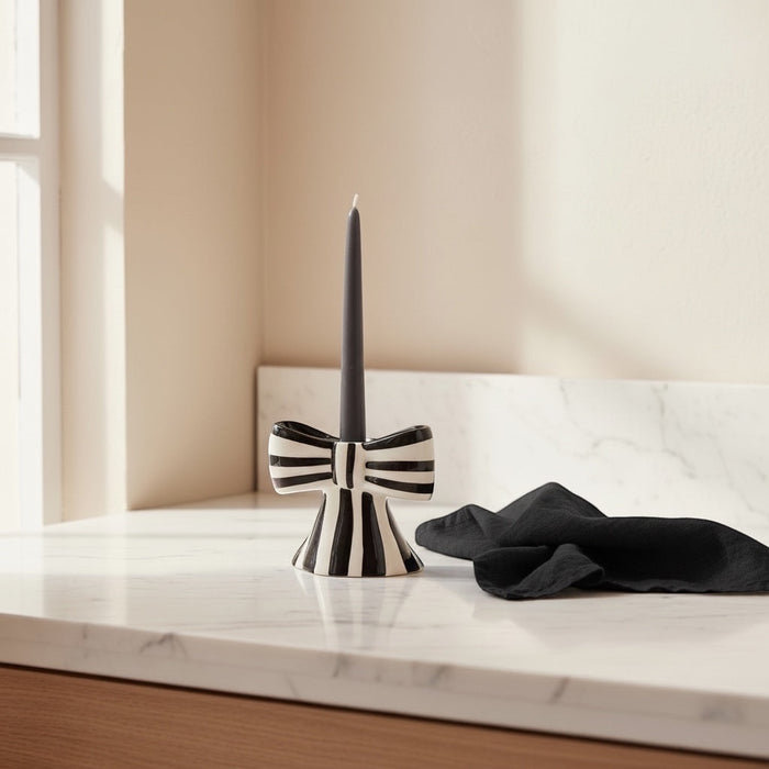 Eclectic black and white striped ceramic bow candle holder with a taper candle on a marble surface.