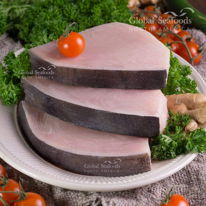 Three raw swordfish steaks on a white plate with tomatoes and leafy greens