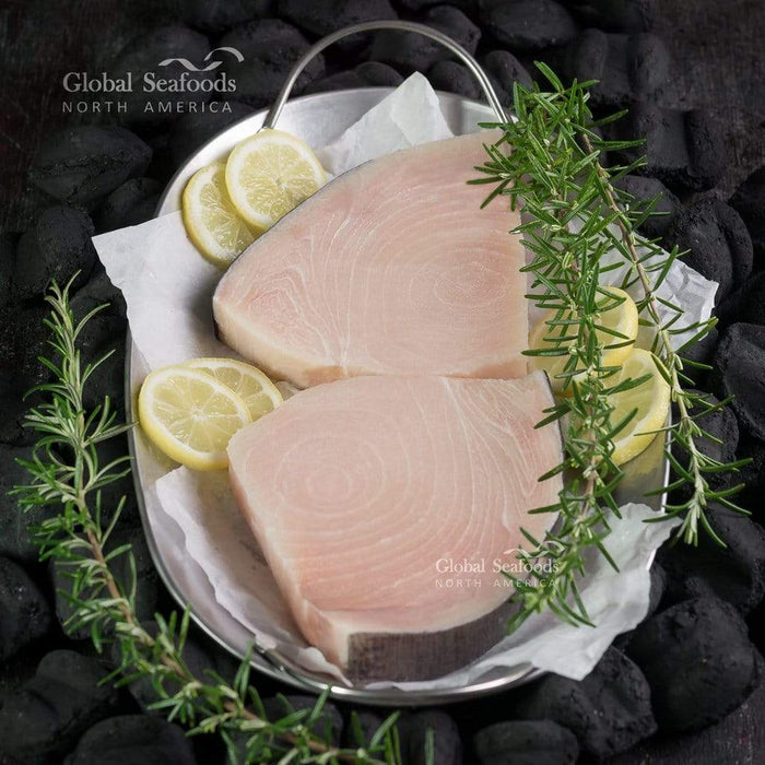 Two raw swordfish steaks on a metal plate with rosemary and lemon