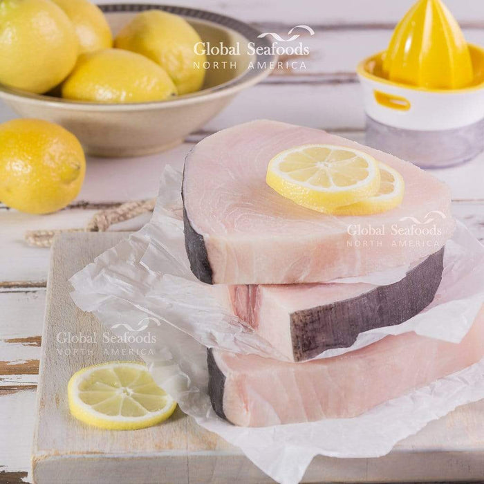 Three raw swordfish steaks stacked with parchment and lemon slices