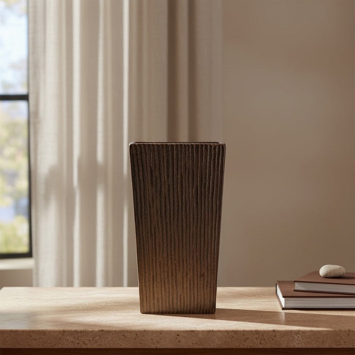 Eclectic earth brown ceramic floor vase with a tall, vertically ribbed architectural silhouette on a wooden table.