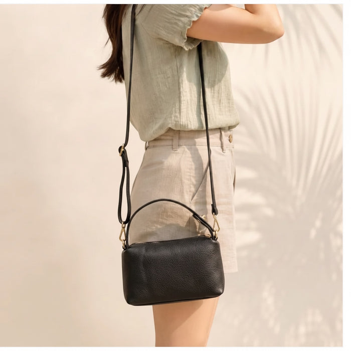 Eclectic black pebbled leather crossbody bag with top handle and gold hardware worn by a woman in a light outfit