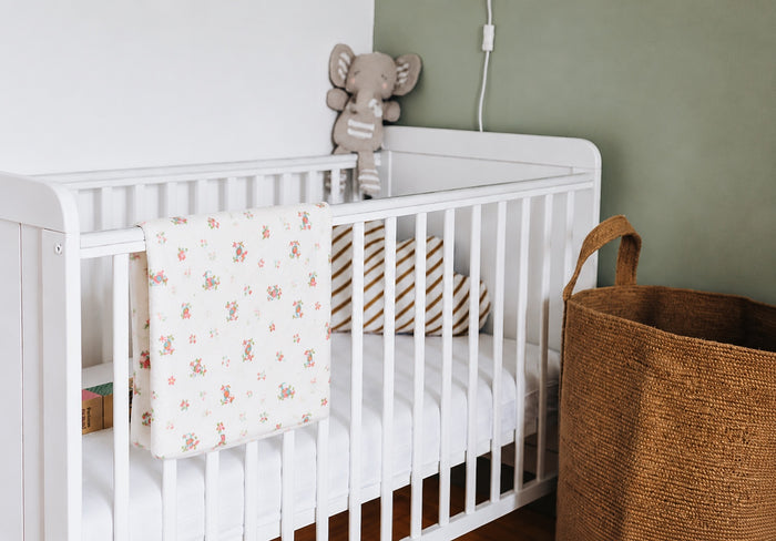 Eclectic Toucan Paradise cotton flannel swaddle draped over a white baby crib in a cozy nursery setting.