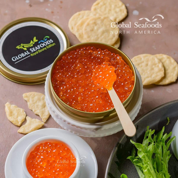 Trout red caviar displayed in a small white bowl, served on a cracker in the front, with an open tin of caviar in the background for an elegant and inviting presentation