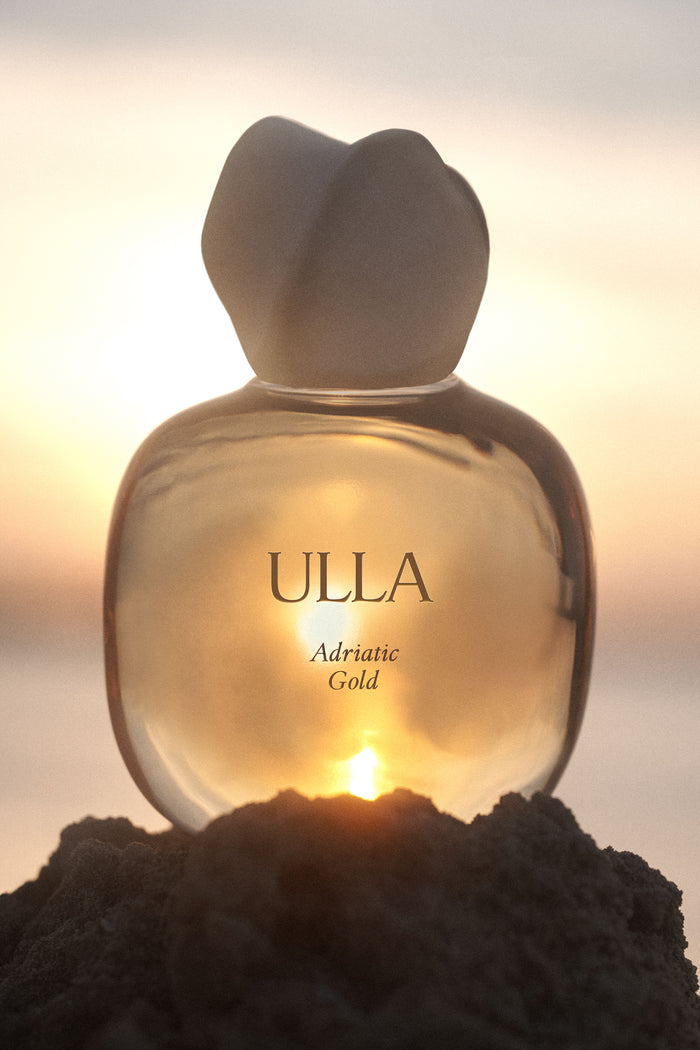 ULLA Adriatic Gold Designer Fragrance Bottle Glowing Against Coastal Sunset - Lifestyle | Ulla Johnson