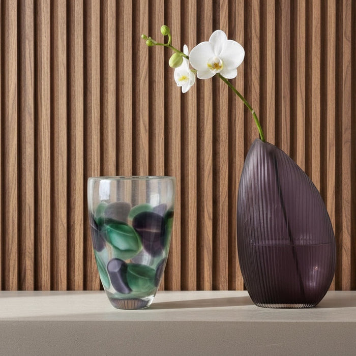 Eclectic violet ribbed glass vase with an asymmetrical silhouette displayed next to a patterned glass vase.