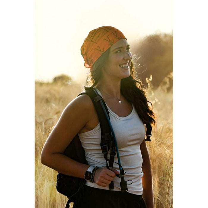 Woman with a backpack and orange headband standing in a field with a warm glow