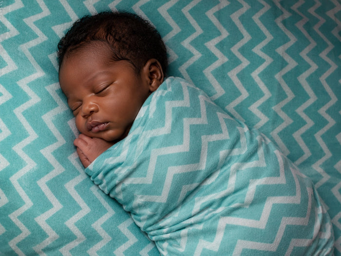 Eclectic baby swaddled in a soft turquoise and white chevron cotton flannel blanket sleeping peacefully